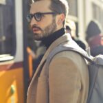 A stylish man with a backpack boards a tram in bustling Budapest, Hungary, during the day.